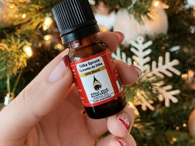 hand holding a bottle of Essential Oils in front of a Christmas tree