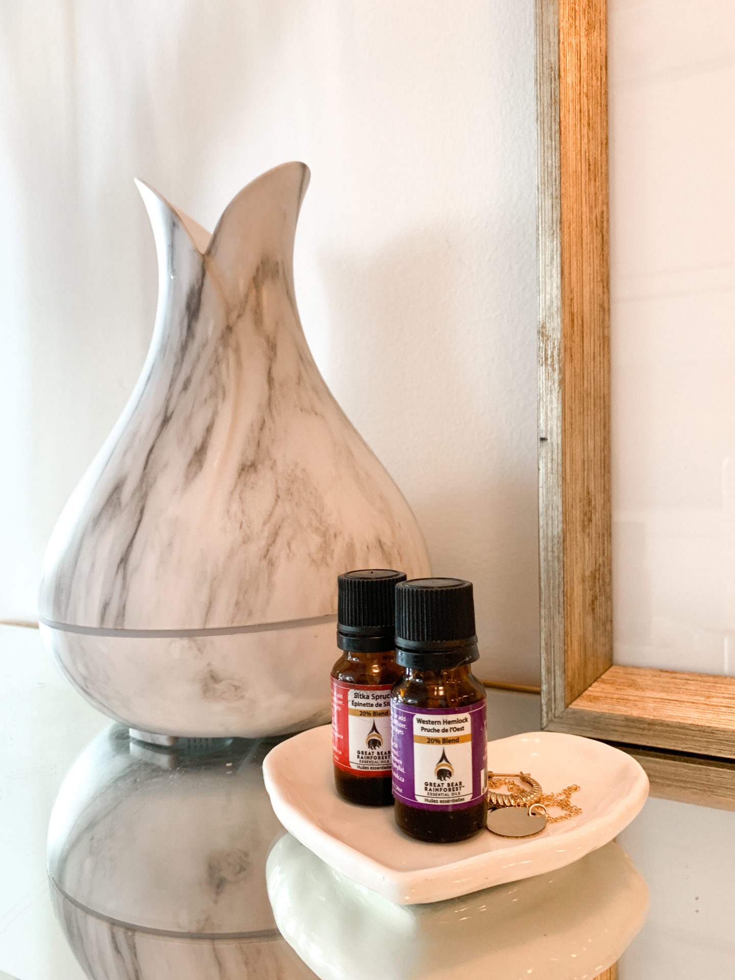 Essential oil bottles sitting beside a diffuser on a dish with jewelery 