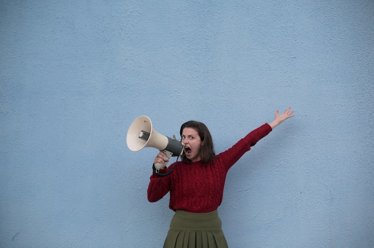 Angry Woman Yelling into a Megaphone in front of a blue wall outside