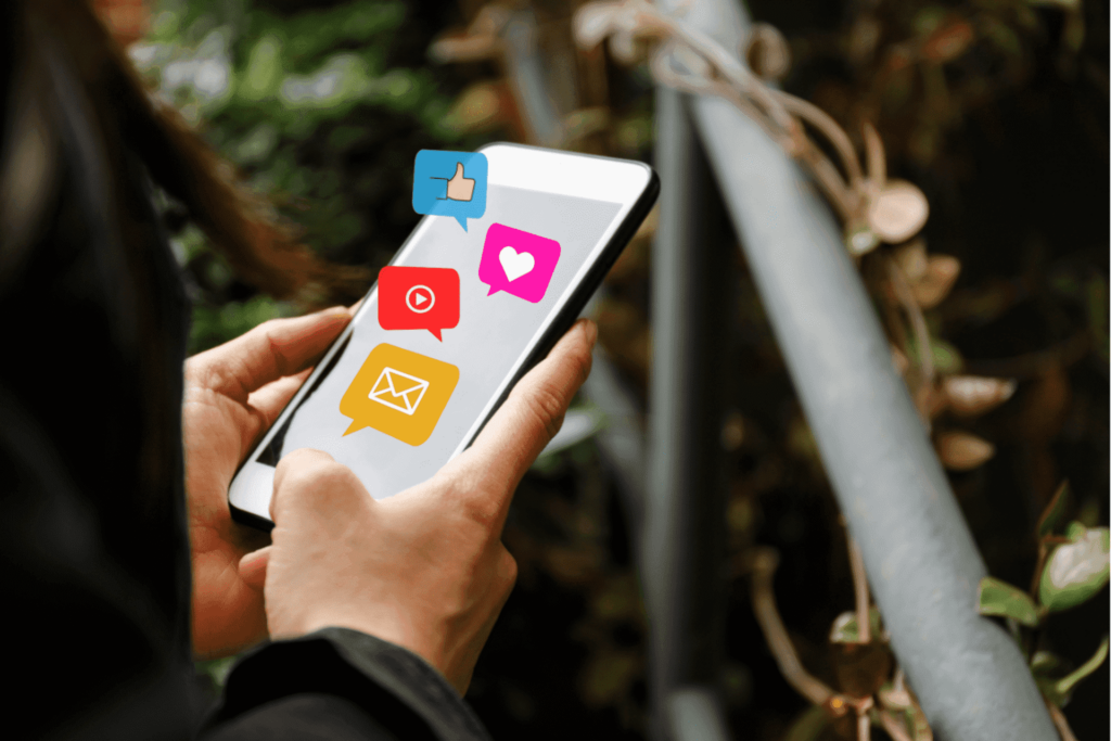Image of floating cartoon icons on the screen of a phone, holding it with both hands.