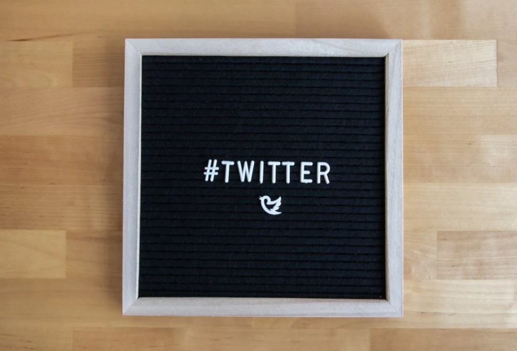 Sign in front of wooden background that says #twitter, with a bird icon