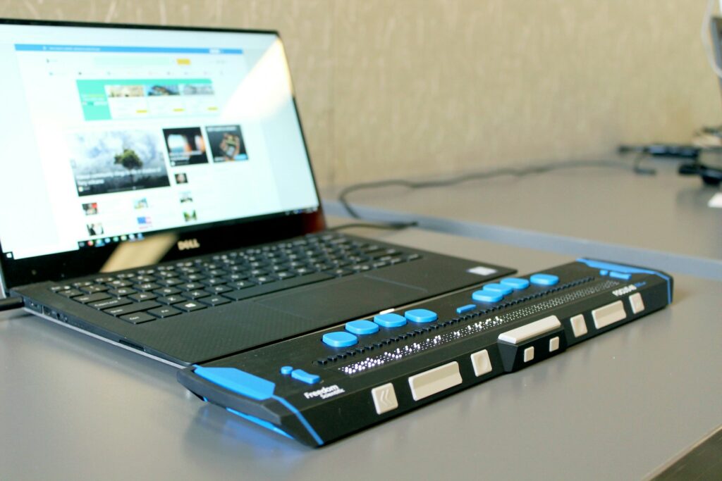 Open laptop with screen reader, on a grey desk.